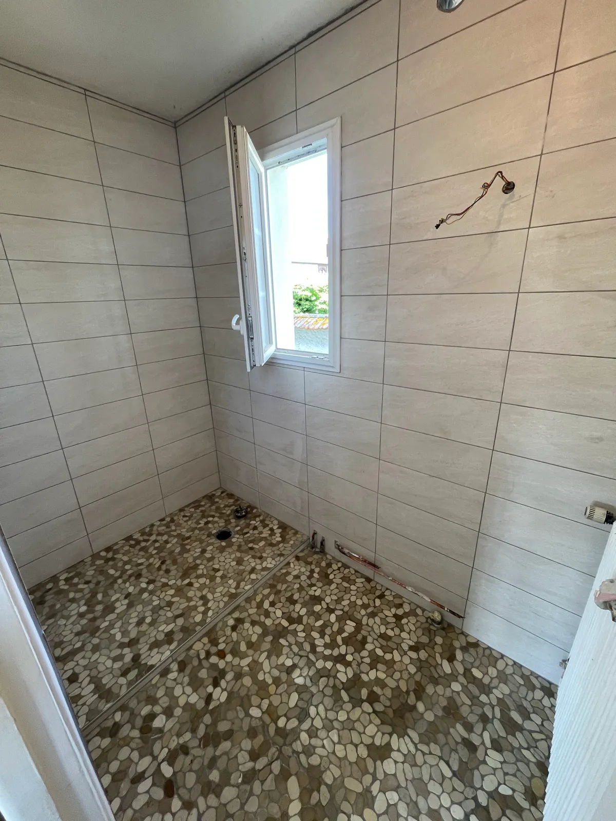 Salle de bains en cours : murs entièrement carrelés, sol et receveur de douche en galets